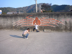 井田のエントリー口に大きく描かれていたタカアシガニの前に立つ石田さんを撮影する鍵井さんを撮影。なんのこっちゃ！